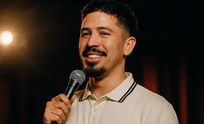 A man with curly hair and a goatee smiles while holding a microphone.