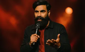 A man with a beard holds a microphone and gestures with his hand while speaking.