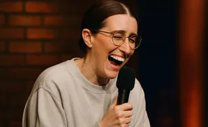 A woman with glasses laughs heartily into a microphone.