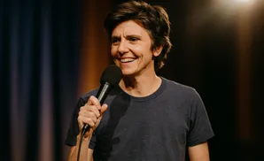 Comedian Tig Notaro smiles while holding a microphone on stage.