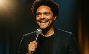Trevor Noah smiles and holds a microphone on stage.