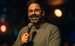 A man with glasses and a beard smiles while holding a microphone.