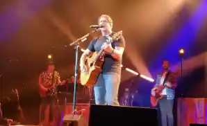 billy currington on stage holding guitar with band behind him.