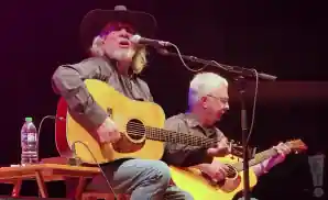 john anderson singing and playing the guitar while sitting.