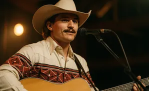 Man in a cowboy hat and western shirt playing guitar and singing into a microphone.