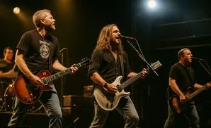 Three men play instruments on a stage at night, bathed in stage lights.