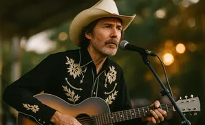 Man in a cowboy hat and embroidered shirt playing an acoustic guitar and singing into a microphone.