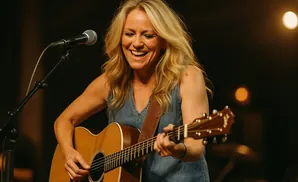 A blonde woman smiles while playing an acoustic guitar at a concert.