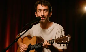 Man singing and playing an acoustic guitar in front of a microphone.