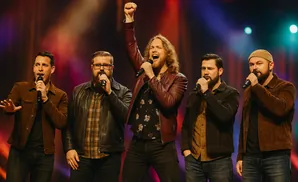 Five men sing into microphones on a stage, one with his fist raised in the air.
