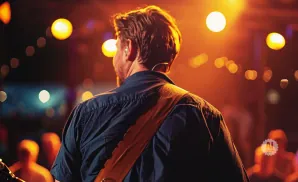 Man with guitar strap on his back, illuminated by stage lights, with bokeh lights in the background.