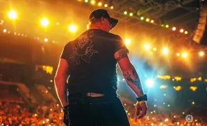 Man on stage with tattooes facing away from camera, illuminated by bright lights and a crowd.