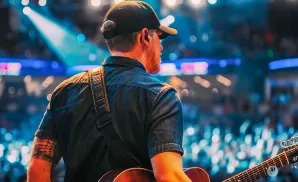 A man in a black cap and t-shirt plays an acoustic guitar and sings into a microphone.