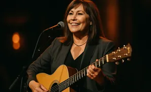 Woman playing an acoustic guitar and singing into a microphone on stage.