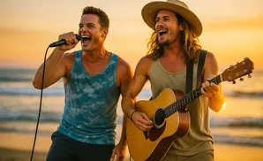 Two men singing and playing guitar on a beach at sunset.