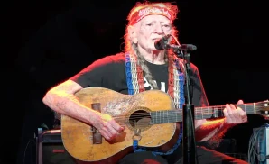 willie nelson performing on stage holding a guitar wearing a red bandana