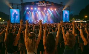 Crowd with hands raised at an outdoor music festival at night.