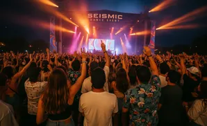 A large crowd cheers with hands in the air at an outdoor concert.