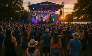 Crowd watches band perform on stage at outdoor festival at sunset.