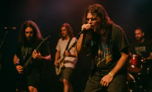 A metal band performs on stage with the lead singer in the foreground.