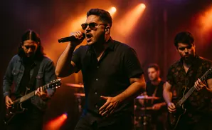 A rock band performs on stage, with the lead singer in the foreground singing into a microphone under bright stage lights.
