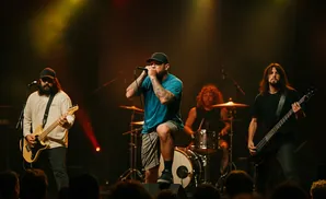 A rock band performs on a dimly lit stage with spotlights highlighting the lead singer and guitarists.
