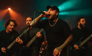 A band performs on stage with dramatic lighting; the lead singer holds a microphone to his mouth.