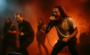 A band performs on stage with red and blue lighting, vocalist in the foreground singing into a microphone.