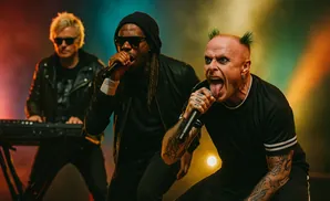 Three musicians on stage. The frontman in front has green spiked hair and his tongue out.