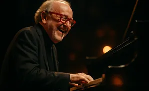 A man with red glasses and a black suit laughs while playing the piano.