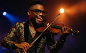 Man in a patterned jacket happily plays the violin under stage lights.