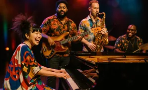 A jazz band performs with a female pianist in front, smiling and playing, while others play bass, saxophone, and drums.