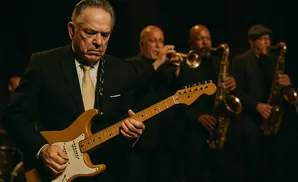 A jazz band plays on stage, with a guitarist in the foreground and saxophonists and a trumpeter in the background.