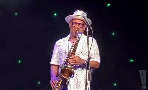 kirk whalum playing saxophone in white dotted polo and white hat