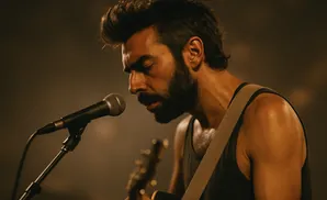 Man with beard playing guitar and singing into a microphone