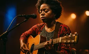 Woman with afro playing an acoustic guitar and singing into a microphone.