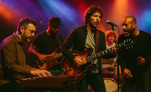 A band performs on stage with a keyboardist, two guitarists, and a singer under colorful stage lights.