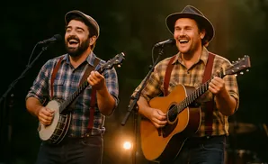 Two men in plaid shirts and suspenders play banjo and guitar, singing into microphones outdoors.