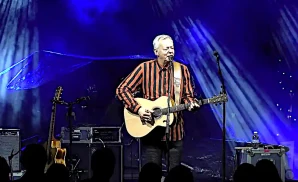 tommy emmanuel playing the guitar and singing while wearing a striped shirt