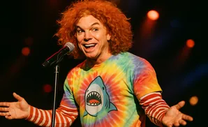 Comedian Carrot Top in a tie-dye shirt with a shark graphic, performing on stage.