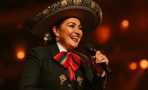 A woman in a mariachi hat and suit smiles and sings into a microphone.