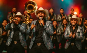 A mariachi band performs on stage, with the lead singer in a patterned jacket and cowboy hat.