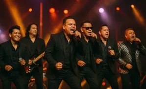 A band of male singers in black suits performs on stage with dramatic lighting.