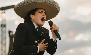 A woman in a mariachi outfit sings passionately into a microphone outdoors.