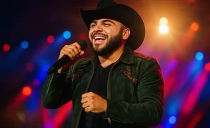 A man in a cowboy hat sings into a microphone on a colorful, illuminated stage.