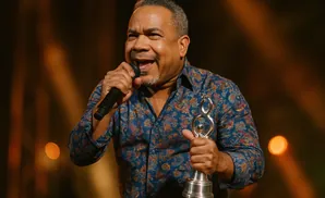 A man in a patterned shirt sings into a microphone while holding an award.