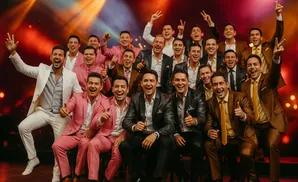 A group of men in matching pink and brown suits pose for a picture with bright lights behind them.