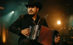 A man in a black cowboy hat and suit plays an accordion on a dimly lit stage.
