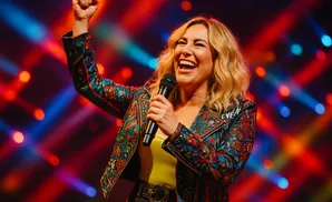 A woman in a colorful jacket sings into a microphone with her fist in the air.