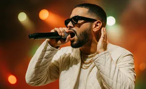 A male singer with sunglasses and gold chains performs into a microphone.